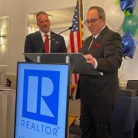 Howard Schaeffer and Chris Raad stand at a podium with the Realtor R logo displayed.